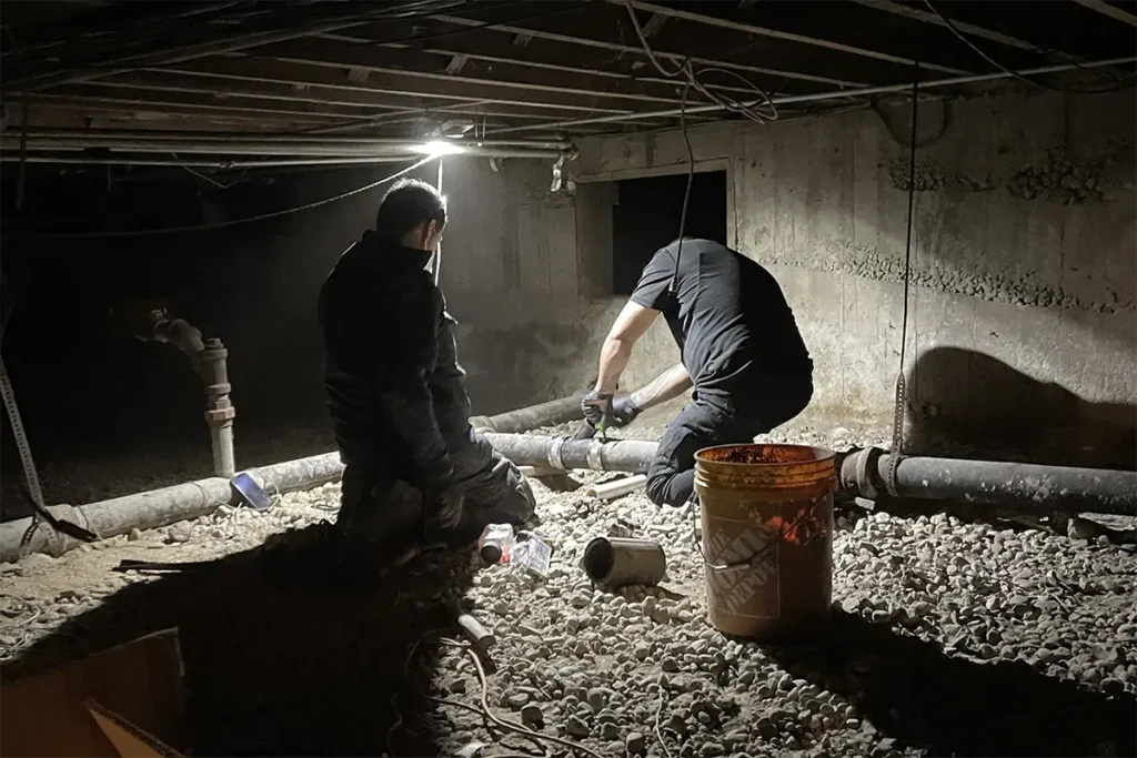 Certified plumbers repairing existing sewer line in basement
